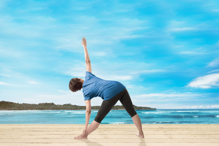 Rear view of asian woman doing yoga on the pierの写真素材