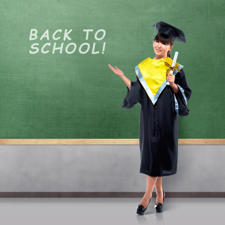 Pretty asian female with graduation caps showing back to school message on the chalkboardの写真素材