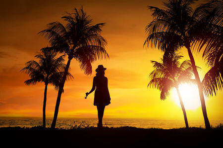 Silhouette of female tourist standing on the beach at sunsetの写真素材