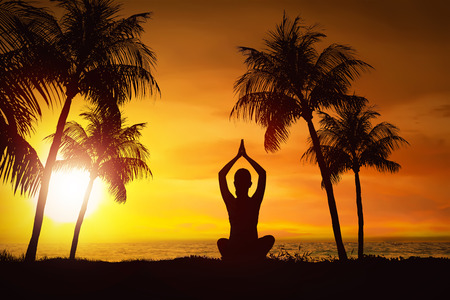 Silhouette of woman doing yoga with ocean view at sunsetの写真素材