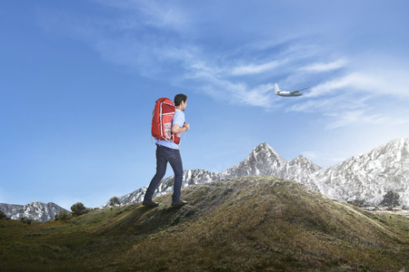 Young asian man with backpack hiking the mountain with blue sky backgroundの写真素材