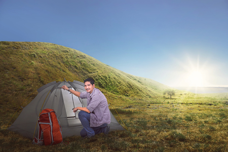 Attractive asian traveler man set up a tent on the grass fieldの写真素材