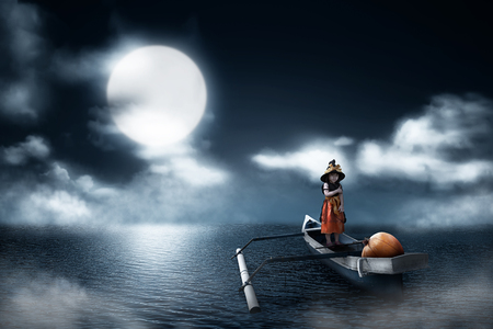Portrait of asian little girl with witch costume and pumpkin on the boat in lake at nightの写真素材