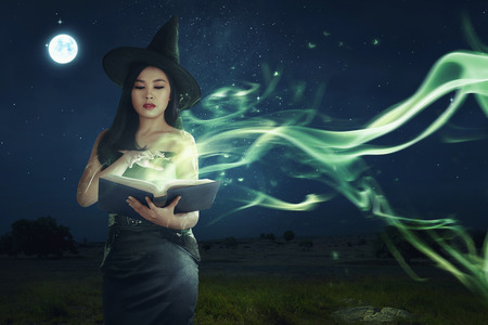 Beautiful asian witch woman learning the magic spell from book on the night