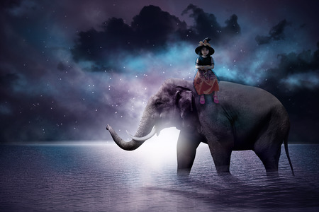 Asian girl sitting on an elephant with dramatic view backgroundの写真素材
