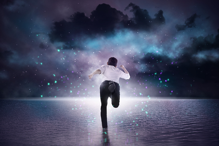 Rear view asian businessman running to the ocean with dramatic sky backgroundの写真素材