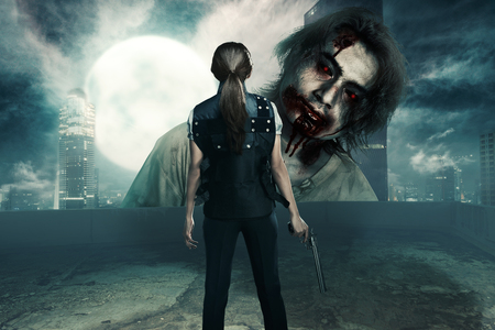 Rear view of asian woman with pistol standing in front of big zombie in the city. Halloween conceptの写真素材