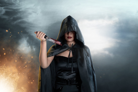 Dark witch with black hooded cloak and knife in her hands. Halloween conceptの写真素材