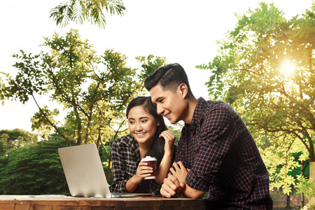 Attractive asian couple watching media on laptop on the park