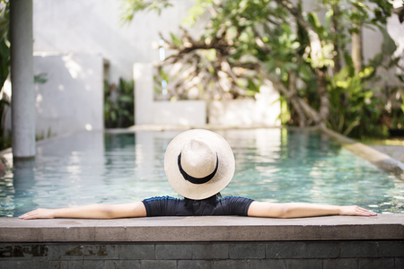 Rear view of asian woman with hat leaning back on the poolsideの写真素材