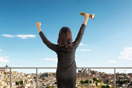 Rear view of asian businesswoman celebrating success with trophy on officeの写真素材