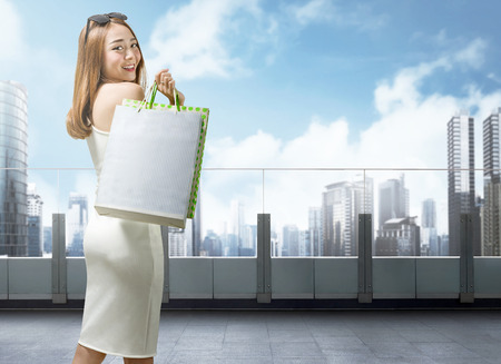 Pretty asian woman in white dress holding shopping bags on mall terraceの写真素材