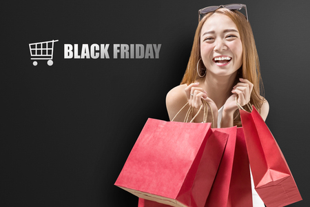 Pretty asian girl holding red paper bags after shopping. Black friday conceptの写真素材