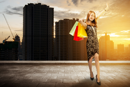 Happy asian woman in black dress holding shopping bags on the city. Black friday conceptの写真素材