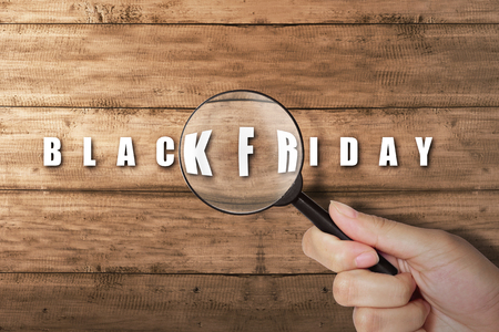 Hand looking at Black Friday text with magnifying glass on wooden tableの写真素材