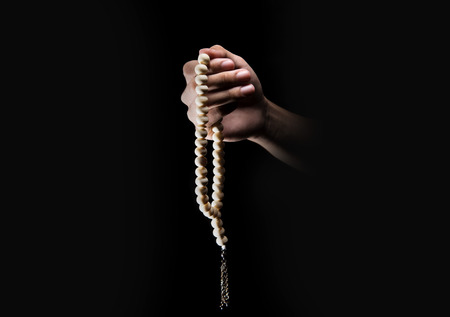 Male hands praying using prayer beads over dark backgroud. Muslim Prayの写真素材