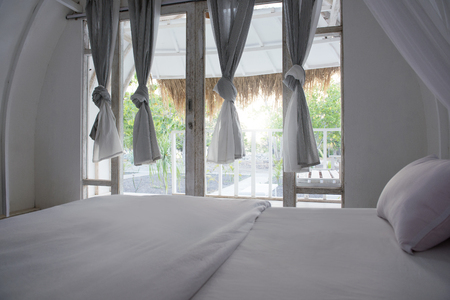 Interior of cottage with bed and curtain on the door. Wooden cottage on Sumbawa, Indonesiaの写真素材