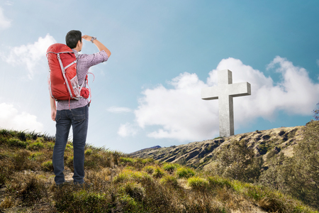 Rear view of asian man with backpack looking at cross on the hillの写真素材