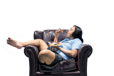 Asian fat man snacking donuts on the couch isolated over white background. Fat man diet conceptの写真素材