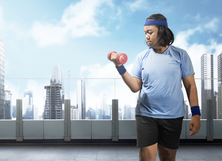 Asian fat man doing exercise with dumbbell on terrace gym. Fat man diet conceptの写真素材
