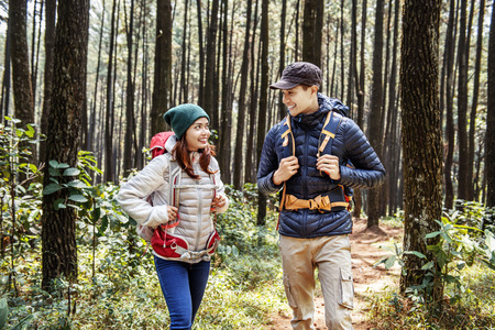 Young asian couple hikers with backpack walking on forest pathの写真素材