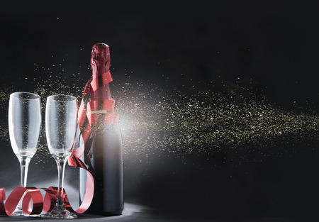 Wine bottle and glasses with red ribbon and golden glitters over black background. New year and celebration conceptの写真素材