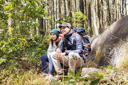 Happy asian couple hikers sit on a tree trunk while resting on the forestの写真素材