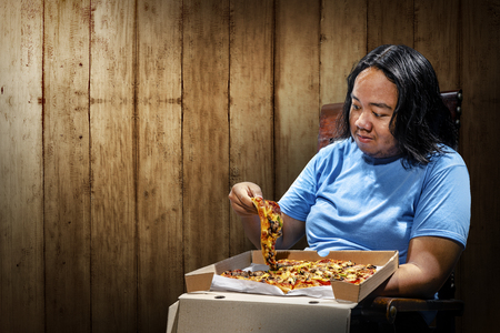 Young asian fat man eating slice of pizza on chair. Fat man diet conceptの写真素材