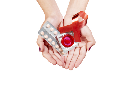 Hands showing wrapped condom and contraceptive medicine with red awareness ribbon isolated over white background. World Aids dayの写真素材