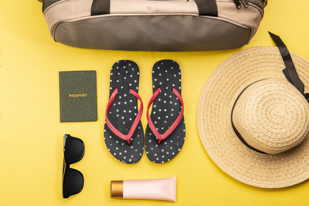 Woman stuff such as luggage bag, hat, slippers, lotion, sunglasses and passport for traveling on yellow background. View from aboveの写真素材