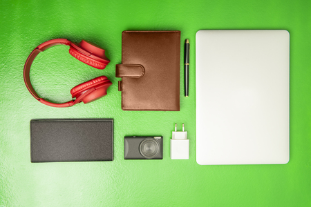 Businessman equipment like laptop, pen, notebook, camera, wallet and headphones for work on green background. View from aboveの写真素材