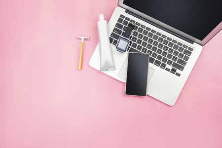 Man stuffs such as laptop, smartwatch, mobile phone, yellow shaver and toothpaste product for traveling on pink background. View from aboveの写真素材