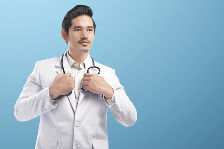 Handsome asian doctor man wearing lab coat and holding stethoscope on his neck over blue backgroundの写真素材