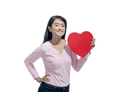 Smiling asian woman holding red heart shape posing isolated over white background. Valentines dayの写真素材