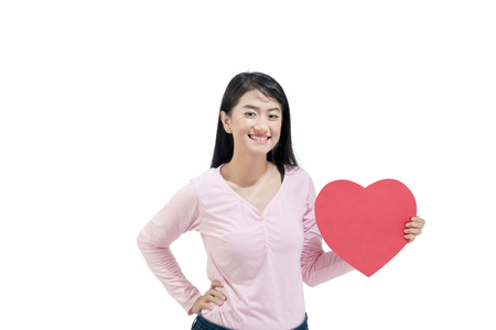 Image of asian woman holding red heart paper posing isolated over white background. Valentines dayの写真素材