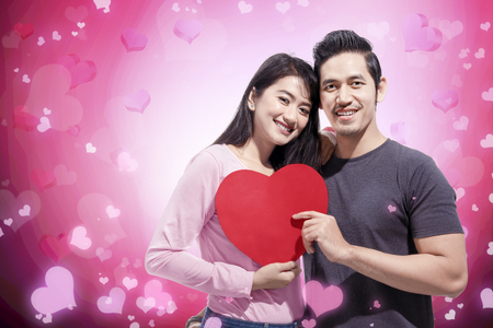 Romantic asian couple in love standing together and holding red heart shape. Love concept and Valentines dayの写真素材
