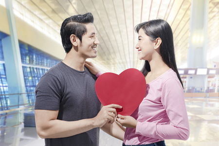 Young asian couple holding red heart shape and looking at one another. Love concept and Valentines dayの写真素材