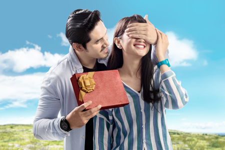 Young asian man covering his girlfriend eyes and giving him a gift. Love concept and Valentines dayの写真素材