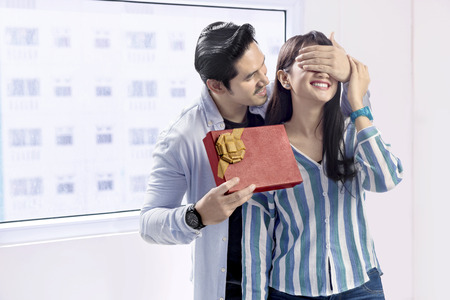Cheerful asian man covering her girlfriend eyes and giving a gift. Love concept and Valentines dayの写真素材