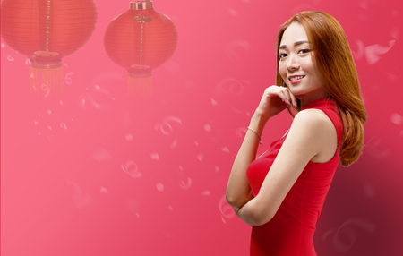 Smiling chinese woman with cheongsam dress standing over red background with lantern. Happy Chinese New Yearの写真素材
