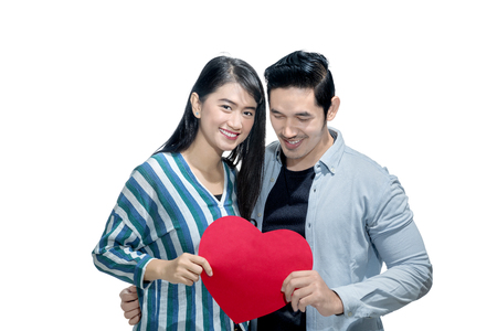 Happy asian couple holding red heart together standing isolated over white background. Love concept and Valentines dayの写真素材