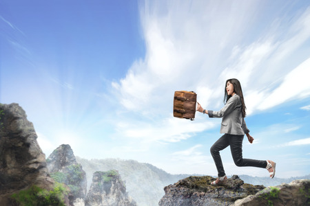 Pretty asian business woman carrying briefcase walking to the top of the mountain. Successful business conceptの写真素材