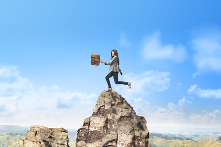 Beautiful asian businesswoman with briefcase walking to the top of mountain. Successful business conceptの写真素材