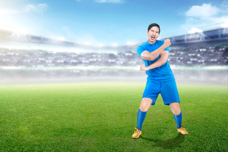 Handsome asian soccer player in blue uniform celebrates victory on stadium backgroundの写真素材
