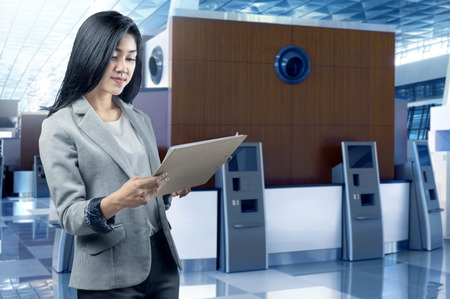 Beautiful asian business woman standing with clipboard inside modern buildingの写真素材