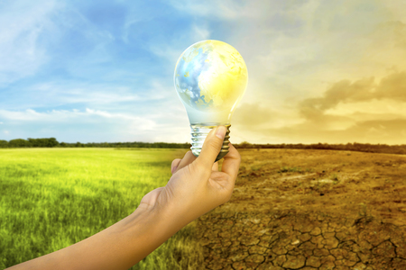 Human hands holding earth inside the light bulb with climate change on the background. Global awareness conceptの写真素材