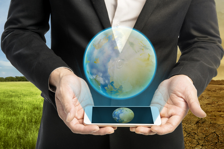Businessman with virtual earth from mobile phone against climate change background. Global awareness conceptの写真素材