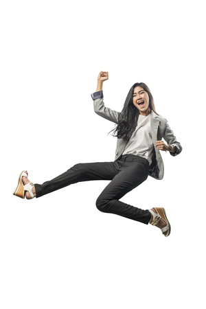 Successful asian business woman jumping and raised arm to the air posing isolated over white backgroundの写真素材