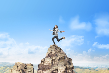 Happy asian business woman jumping on top of the mountain. Successful business conceptの写真素材