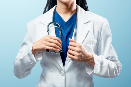 Female doctor with white coat holding stethoscope on her neck over blue backgroundの写真素材